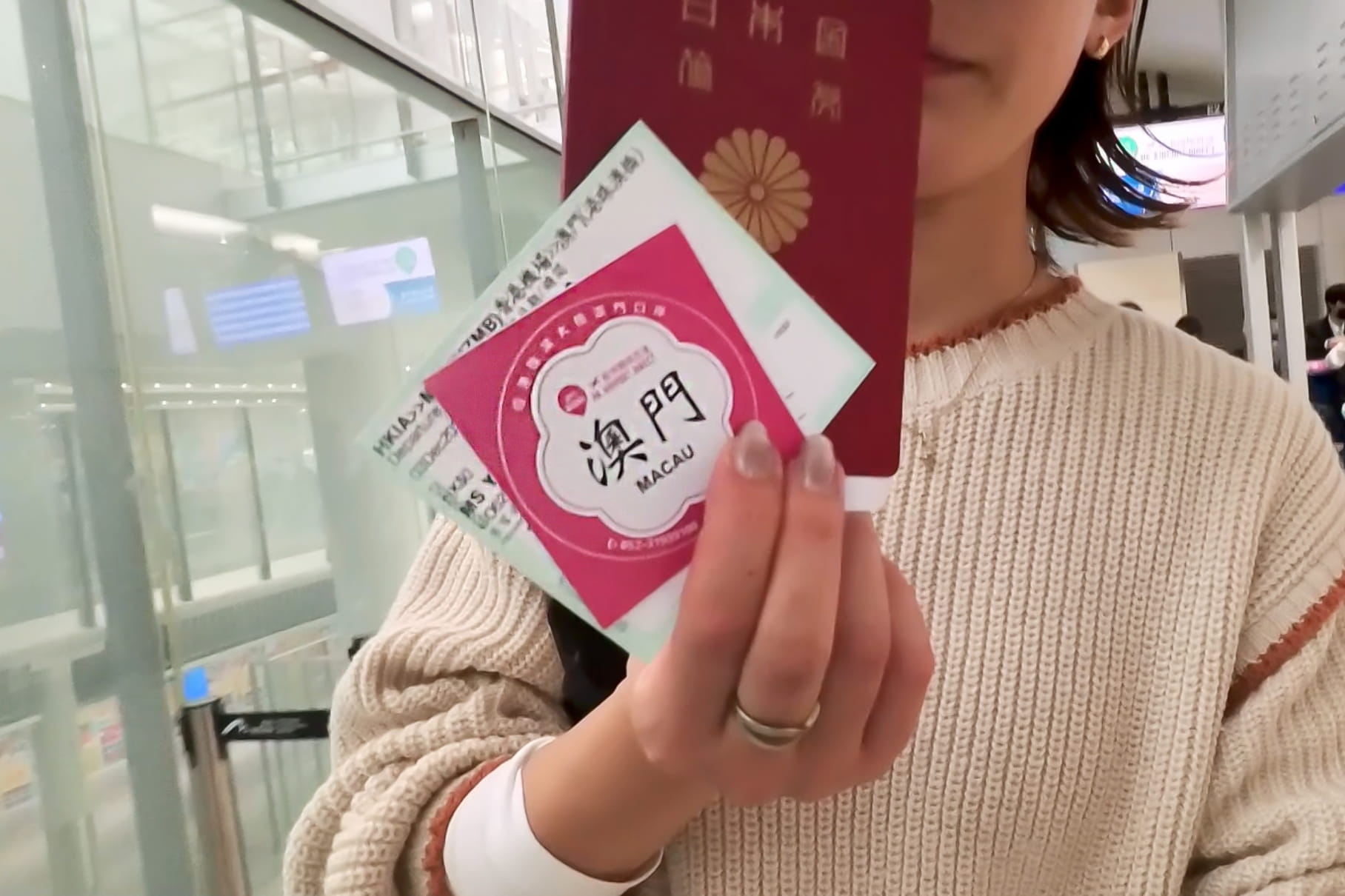 「澳門（MACAU）」と書かれたピンクのチケット、日本のパスポート、搭乗券を手に持つ女性。空港でのマカオ旅行の出発シーン